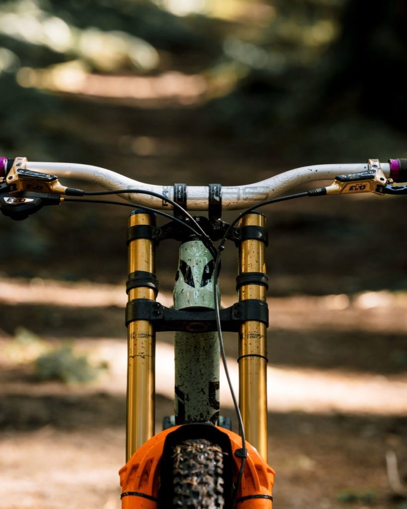Front view of a high-performance downhill mountain bike cockpit and dual-crown suspension fork on a forest trail.