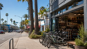 A bright daytime view of a modern bike shop in Santa Monica with several bicycles parked outside, palm-lined streets, and a clean coastal urban setting under a clear blue sky, showcasing a welcoming destination for cyclists and visitors